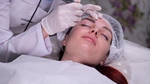 Salon de beauté confortable. Procédure maquillage permanent. Sur le canapé, le patient esthéticien met de la peinture sur ses sourcils. Mo lent 4K — Video