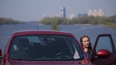 Kız kırmızı bir arabada oturur, kapıyı açar, arabadan iner ve anahtarları gösterir. 4k Yavaş Mo