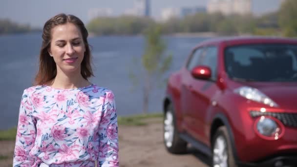 Une jolie fille se tient devant la voiture, vomissant des clés, les attrapant et les agitant dans le cadre. Mo lent 4K — Video