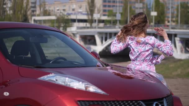 Una chica baila delante de un coche nuevo, se acuesta en el parabrisas y abraza el coche. 4K Slow Mo — Vídeo de stock