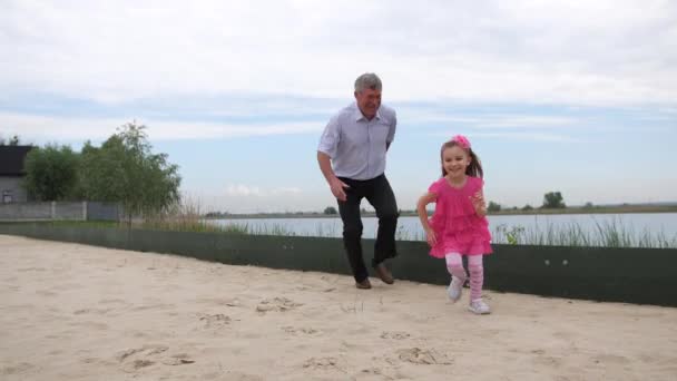 Grootvader vangt aan met haar kleindochter. De familie speelt op het strand. Ze lopen naar de camera. 4k slow mo — Stockvideo