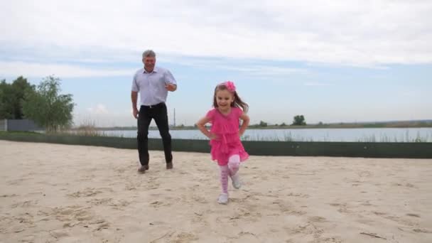 Wnuczka i dziadek biegną wzdłuż plaży. Uśmiechają się i bawią. 4K slow mo — Wideo stockowe