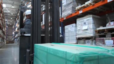 Depodaki standlar boyunca bir kutu ile bir forklift sürmek. 4k Yavaş Mo