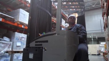 Büyük bir depo. Forklift rafa mal koyarak platformu düşürür ve uzak sürücüler. 4k Yavaş Mo