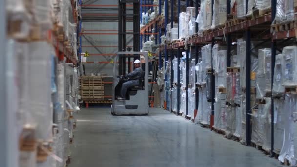 Uma empilhadeira dirige ao longo de enormes estandes com mercadorias em um armazém logístico. 4K Mo lento — Vídeo de Stock