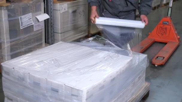 Egy férfi csomagolási termékeket a celofán egy logisztikai raktárban. 4k lassú Mo — Stock videók