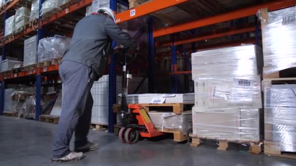 Magazijnmedewerker plaatst pallets. Een man werkt met een handmatige vorkheftruck. 4k slow mo — Stockvideo