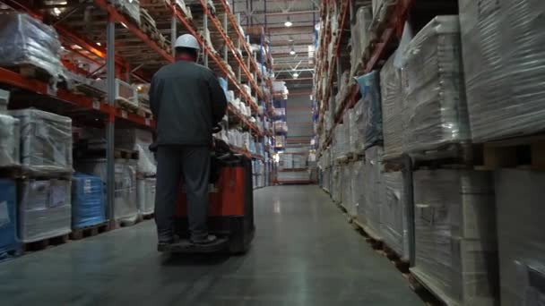 El trabajador monta en la plaza entre los estantes llenos de cajas de mercancías. 4K Slow Mo — Vídeo de stock