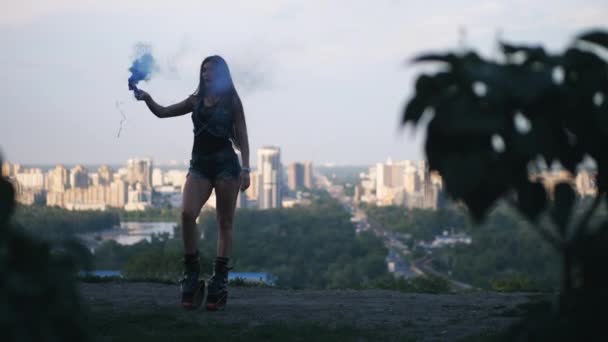 Dziewczyna tańczy w angoo skacze buty w tle miasta. Ma niebieski moduł sprawdzania dymu w rękach. 4K slow mo — Wideo stockowe