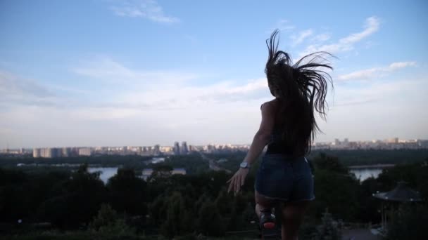 Девушка запрыгивает в сапоги и прыгает, спиной к камере перед ней открывается вид на город. 4K Slow Mo — стоковое видео