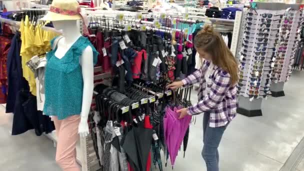 Kvinnan väljer ett paraply i Hypermarket. Flickan tar ett rosa paraply, öppnar den och snurrar under den. 4K långsam Mo — Stockvideo