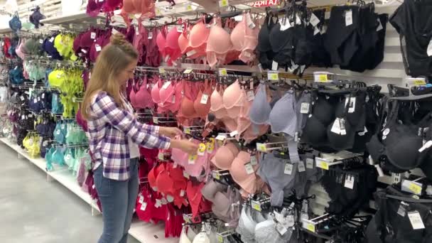Vacker ung kvinna som försöker på en behå i en underkläder avdelning i en stormarknad. 4K långsam Mo — Stockvideo