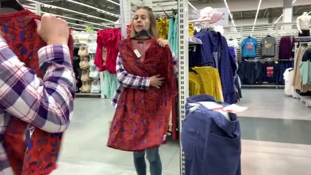 Grande loja. A menina olha para si mesma no espelho, veste seu vestido e chapéu e sorri docemente. 4K Mo lento — Vídeo de Stock