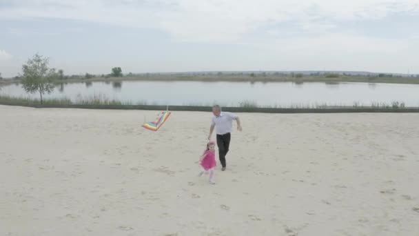 Abuelo y nieta lanzan una cometa en la playa en el lago. Filmando desde el aire. 4K Slow Mo — Vídeos de Stock