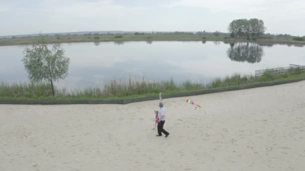 De overspanning van de camera over het strand, die een kleindochter met een grootvader met een vlieger in hun handen loopt. 4k slow mo — Stockvideo