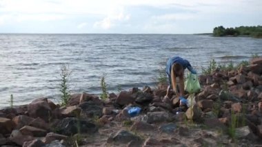 Plastikle kirletilmiş deniz kıyısı. Gönüllü bir kadın çöpü torbaya koyar. 4k Ağır çekim