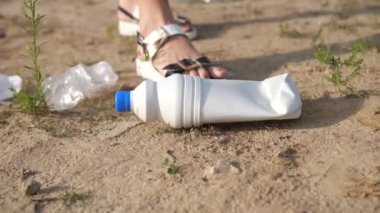 Yakın plan. Bir kadın yerden plastik bir şişe kaldırır ve onu bir torbaya koyar. Gönüllü plastikten sahili temizler. 4k Ağır çekim