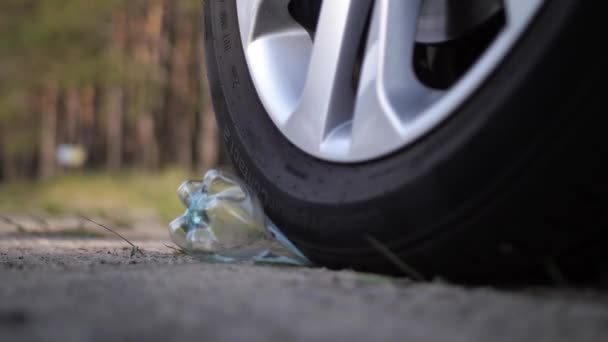 Gros plan. Une bouteille en plastique est allongée sur la route, la voiture déplace la bouteille avec une roue. Mo lent 4K — Video