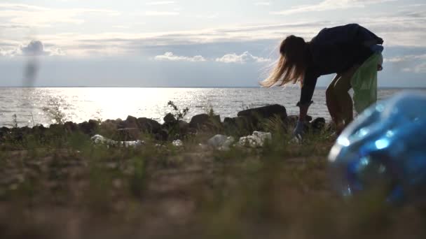 Plastik şişelerle kirletilmiş deniz kıyısı. Genç bir kadın çevreyi temizliyor.. — Stok video