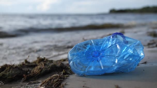 Una botella de plástico se encuentra en la orilla del mar. Las olas golpearon la orilla. Playa contaminada. 4K Slow Mo — Vídeo de stock