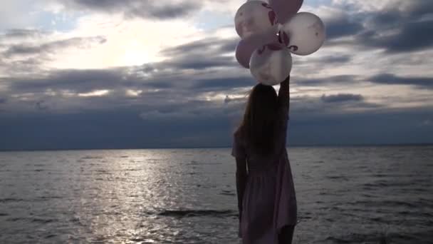 Het meisje in de jurk kijkt naar de zee, in haar handen zijn veel ballen. 4k Slow Mo — Stockvideo
