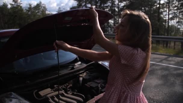 Die Blondine öffnet die Motorhaube eines roten Autos und versucht zu verstehen, was auf der Strecke kaputt ging. 4k langsam mo — Stockvideo