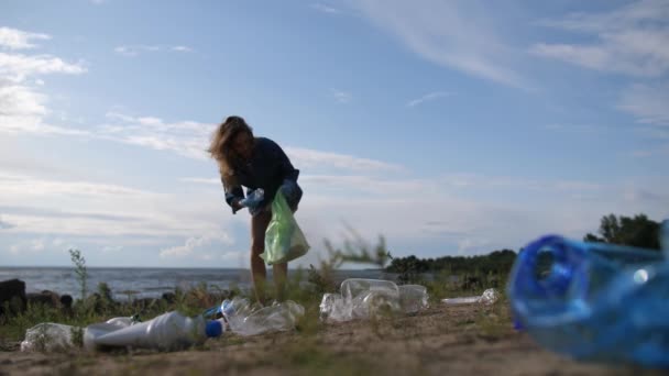 Egy fiatal nő takarítja a tengerpartot. Műanyag palackok, lemezek és berendezések vannak szétszórva az egész országban. 4k Lassú Mo — Stock videók