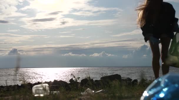 Förorenad strand med plastavfall. En flicka går in i ramen och tar bort allt skräp. 4k Långsam Mo — Stockvideo