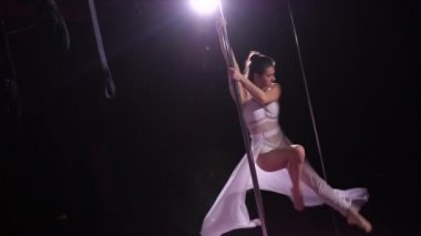 Siyah bir stüdyoda beyaz elbiseli bir dansçı direğin üstünde dans ediyor. Çok nazik hareketler. 4k Ağır çekim
