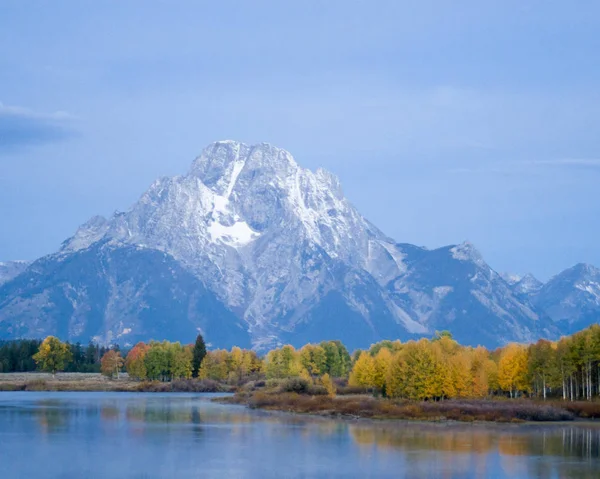 Snow-capped Grand Tetons provide a backdrop for a lazy river refelcting autumn color