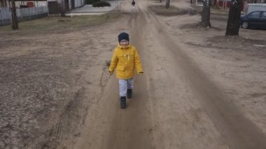 sarı ceket ve şapkalı çocuk küçük bir kasabanın sokaklarında yürüyor