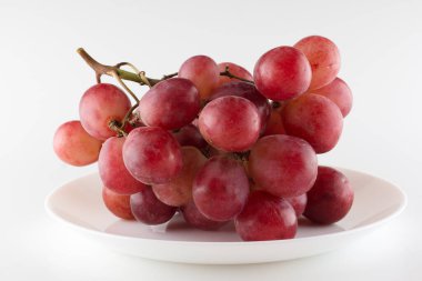 Taze üzümler yemek tabağında beyaz bir sırtüstü uzanır.