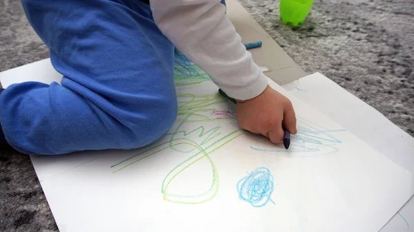 Dziecko uczy się rysować kredki woskowe na podłodze. — Zdjęcie stockowe