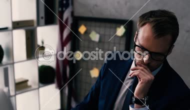 takım elbise ve çene üzerinde elini tutarak ve işyerinde otururken düşünme gözlük yakışıklı işadamı