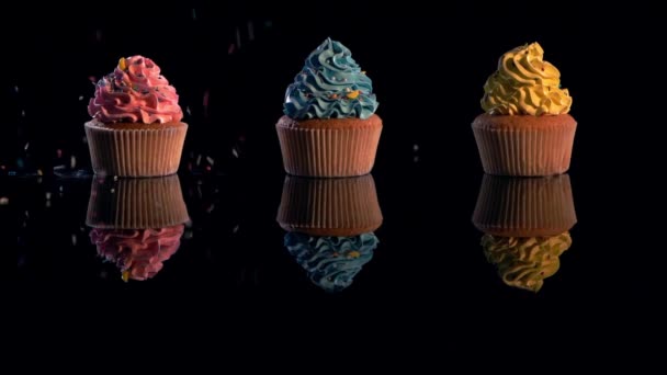 在黑色背景上的五彩纸杯蛋糕上掉落的含糖洒水的慢动作 — 图库视频影像
