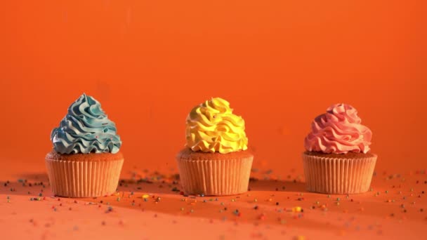 在橙色背景上的五彩纸杯蛋糕上掉落的含糖洒水的慢动作 — 图库视频影像