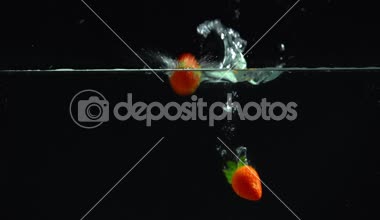 parlak kırmızı çilek içine düşme berrak su siyah arka plan üzerine 