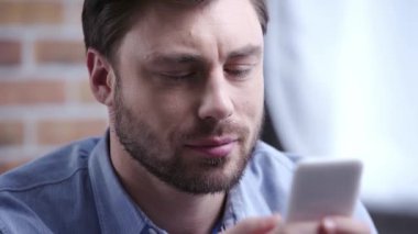 Kaydırma ve Smartphone'da yazarak mavi gömlekli yakışıklı konsantre esmer iş adamı