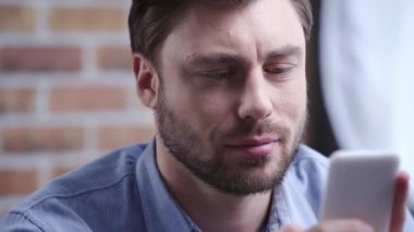 Yakışıklı işadamı smartphone, kullanarak yanıp sönen ve uzağa yavaşça bakarak gülümsemek