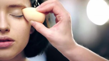 kozmetik sünger ile model göz kapağı na kapatıcı uygulayan makyaj sanatçısı kırpılmış görünümü