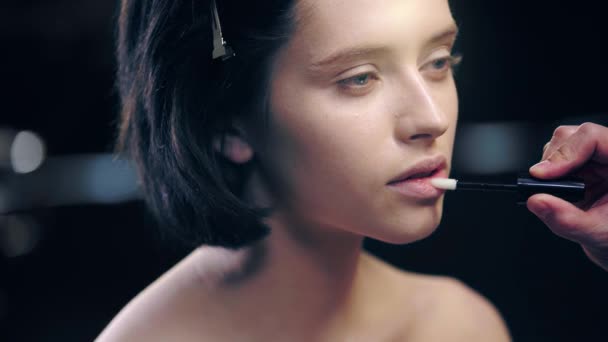 化粧品ブラシでモデルの唇に光沢のあるリップグロスを適用するメイクアップアーティストの部分的なビュー — ストック動画