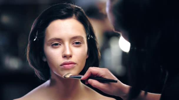 化粧品ブラシでモデルフェイスに光沢のある蛍光光を適用するメイクアップアーティスト — ストック動画