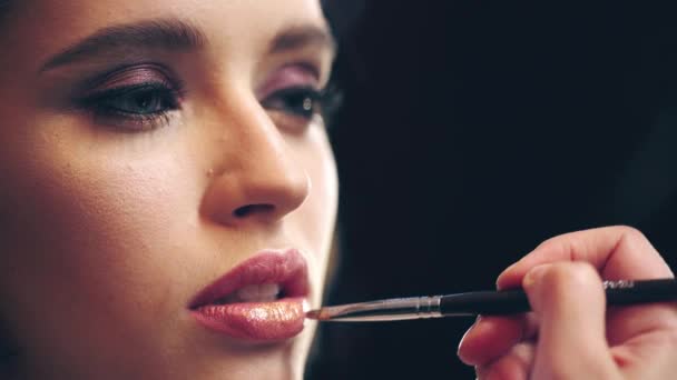 黒で分離されたモデルの唇にリップグロスを適用するメイクアップアーティストの部分的なビュー — ストック動画