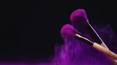 siyah arka plan üzerinde renkli mor holi boya sıçramaları yapma ve kozmetik fırçalar yavaş hareket ateş