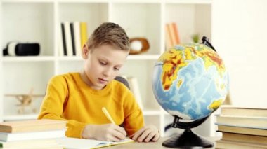 ödev yaparken not defterine yazma ve küreye bakan öğrenci 