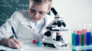 dizüstü bilgisayarda çocuk yazma seçici odak ve sınıfta sıvı ile test tüpleri yakın mikroskop ile bakarak 