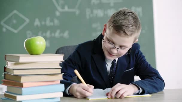 Colegial Feliz Gafas Escribir Cuaderno Cerca Libros Manzana Mientras Que — Vídeo de stock