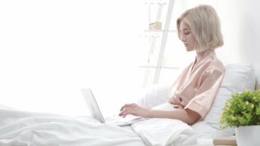yatakta otururken dizüstü bilgisayar ve dokunmadan saç kullanarak çekici sarışın blogger 