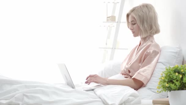 有吸引力的金发博客使用笔记本电脑和触摸头发 而坐在床上 — 图库视频影像
