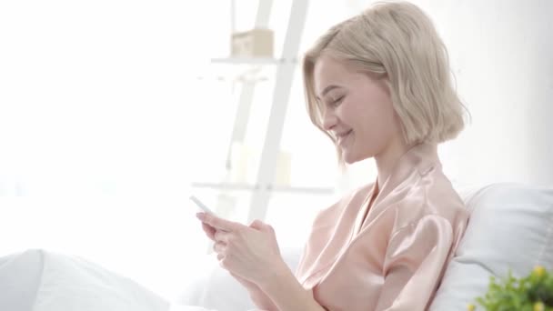 Hermosa Chica Rubia Usando Smartphone Sonriendo Cubriendo Boca Riendo Dormitorio — Vídeos de Stock